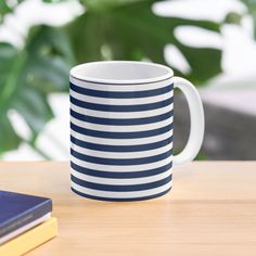 a blue and white striped coffee mug sitting on top of a wooden table next to a book