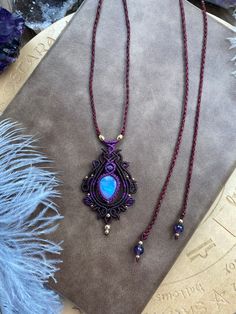 two necklaces are sitting on a table next to a blue feather and purple beads