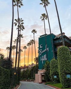 palm trees line the street in front of an apartment building at sunset, with a sign that reads the beverly hotel