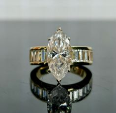 an engagement ring with a pear shaped diamond and baguettes around the band, on a reflective surface