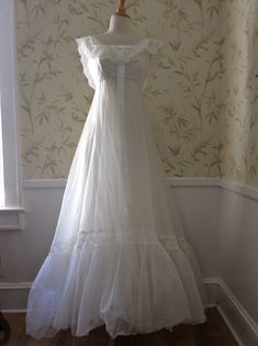 a white wedding dress hanging on a mannequin in front of a wallpapered room