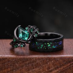 two rings with green and blue stones on them sitting on top of a wooden table