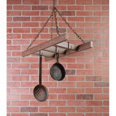 pots and pans hanging from a wooden rack on a brick wall with chains attached to it