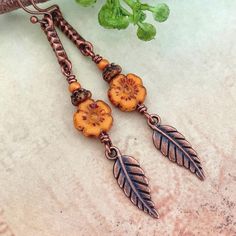 These orange Czech glass flower & leaf earrings feature 1/4" beautifully aged pumpkin orange glass hibiscus flowers. They are 3d - same on both sides. They are attached to rustic hammered connectors & adorned with tiny brown pressed glass flower beads & pumpkin orange seed beads. Dangling freely below these are antiqued copper leaf / feather charms. Total drop is 2 1/8". These are extremely lightweight. All metal components are hypoallergenic non-tarnish to prevent any skin sensitivity. Processi Copper Drop Earrings With Flower And Ear Wire, Copper Drop Flower Earrings With Ear Wire, Bohemian Czech Glass Dangle Flower Earrings, Nickel-free Copper Flower Drop Earrings, Bohemian Flower Czech Glass Earrings, Bohemian Czech Glass Flower Earrings, Bohemian Flower Earrings With Czech Glass, Orange Bohemian Drop Earrings, Orange Bohemian Drop Earrings Jewelry