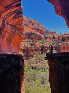 a person sitting on the edge of a cliff looking out at some mountains and trees