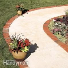 a large planter filled with lots of flowers on top of a brick walkway next to a lush green field