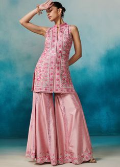 Featuring a pink silk sleeveless kurta with band collar neckline, embellished with gota, zari and mirror applique work. Paired with an embellished garara bottoms and a matching organza dupatta with cutwork border detailing and tassels on hem. An absolute fusion silhouette for Sangeet and Engagement parties. Composition : Kurta & Garara: Slub Silk, Dupatta: Organza Care: Dry Clean Only and Vacuum Storage All products can be customised for sleeves, length of blouse and neck design Delivery : 6-8 weeks as the product is hand crafted. Check Size Guide or choose MySize for free customisation (All Sizes above XL can be made at 15% additional cost) For more information and sizes please contact fabiliciousfashion@gmail.com or visit our Copenhagen studio. Sleeveless Chanderi Bollywood Palazzo Set, Sleeveless Chanderi Palazzo Set For Navratri, Bollywood Style Sleeveless Chanderi Palazzo Set, Designer Sleeveless Kurta With Mirror Work, Chanderi Anarkali Sharara, Sleeveless Anarkali Kurta With Gota Work, Sleeveless Sharara With Zari Work For Eid, Pink Sharara With Zari Work Sleeveless, Sleeveless Resham Embroidery Sharara For Festivals