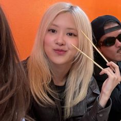 a woman holding chopsticks in front of her face while sitting next to a man