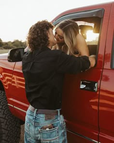 a man and woman kissing in the back of a red truck with their hands on each other's butts