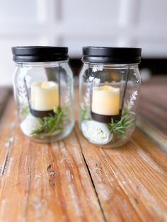 two jars with candles and flowers in them sitting on a wooden table next to each other