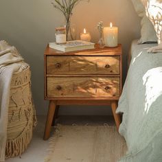 a nightstand with two candles on top of it next to a bed and a blanket