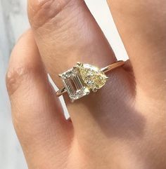 a woman's hand holding an engagement ring with two stones on it and the center stone is yellow gold