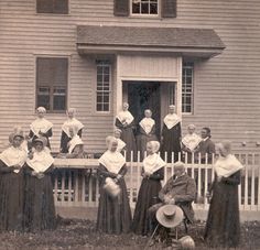 an old black and white photo of women in front of a house with their hats on