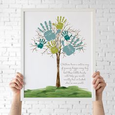 a person holding up a handprinted tree with blue and green hands on it