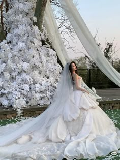 a woman in a wedding dress standing next to a tree with white flowers on it