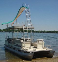 a pontoon boat with a slide on the back is parked at the edge of a body of water