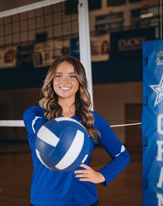 a woman is holding a volleyball in front of a net and smiling at the camera