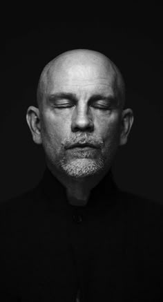 a bald man with his eyes closed in black and white, staring at the camera