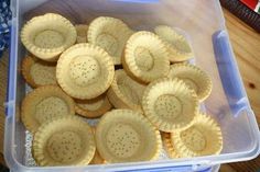 a plastic container filled with small pies on top of a wooden table next to a knife