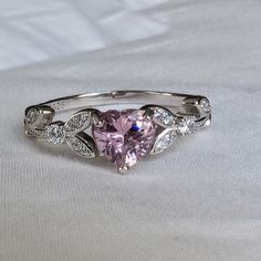 a pink heart shaped diamond ring with white diamonds on it's sides and the center stone is surrounded by leaves