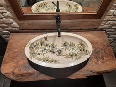 a bathroom sink with an olive design on the bowl and mirror above it, in front of a brick wall