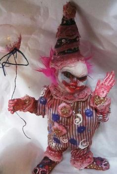 a creepy clown doll with pink hair and makeup on it's face holding a string