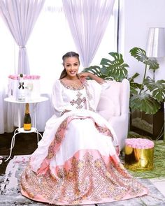 This stunning dress is a true masterpiece of Ethiopian textile art. The lower part of the dress is made from shimena, a handwoven fabric known for its intricate patterns and rich texture. The shimmering material adds a touch of elegance and movement to the dress, making it perfect for special occasions. The dress is adorned with light pink tilf embroidery, a traditional Ethiopian technique that involves intricate and colorful designs stitched onto fabric. The tilf embroidery on this dress is par Festive Embroidered Habesha Kemis For Eid, Festive Bohemian Embroidered Habesha Kemis, Festive Traditional Handloom Habesha Kemis, Traditional Festive Habesha Kemis, Handloom, Festive Folk-style Habesha Kemis, Eritrean Dress, Habesha Kemis, Handwoven Fabric, Light Pink Color