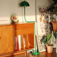 a green lamp sitting on top of a wooden cabinet next to a potted plant