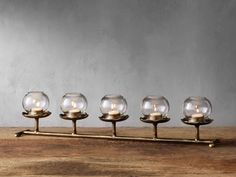 four glass candles sitting on top of a wooden table next to a metal holder with gold handles