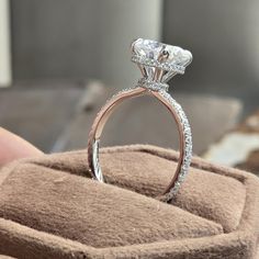 a close up of a diamond ring on a cushioned surface with a person's hand holding it