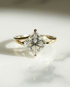 a gold ring with a princess cut diamond in the center on a white table top