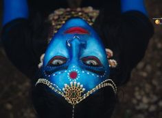 a woman with blue face paint on her face and hands behind her head, looking down at the camera