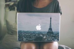 a woman is sitting on her bed with an apple laptop in front of her face