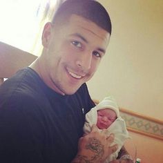 a man holding a baby in his arms and smiling at the camera while wearing a black shirt