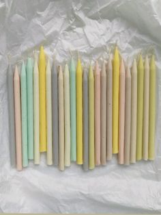 many candles are lined up on a sheet of wax paper, with one yellow candle in the middle