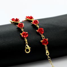 a pair of red roses are attached to a gold chain bracelet on top of a black cloth