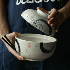 a person holding two bowls with chopsticks in their hands and the bowl has black speckles on it