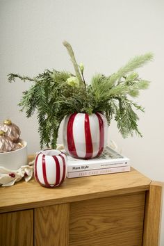 a red and white striped vase sitting on top of a wooden table next to a book