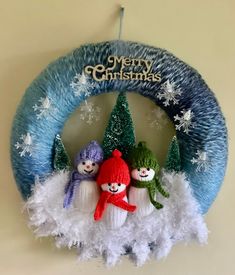 three knitted snowmen sitting on top of a blue wreath