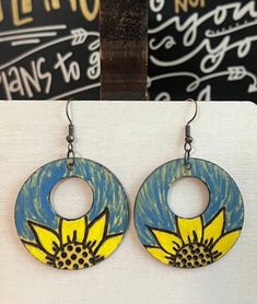 a pair of earrings with yellow and blue flowers painted on the inside of them, hanging from metal hooks