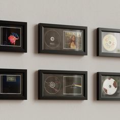 several framed pictures are hanging on the wall with cd's in them and one has a disc