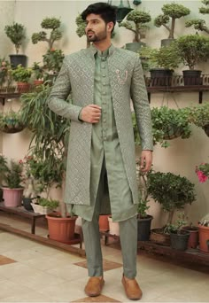 a man standing in front of potted plants wearing a green suit and black hat