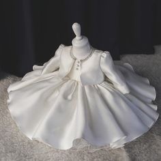 a white dress on display in front of a black background with the back of it's dummy