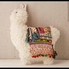 a llama stuffed animal is standing next to a wall with a decorative pillow on it's back