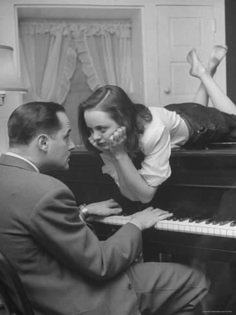 a black and white photo of a woman laying on top of a piano next to a man