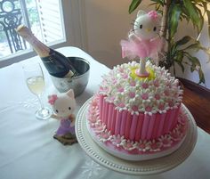 a hello kitty cake with pink icing and white frosting on top, next to a bottle of champagne