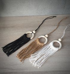 three necklaces with beads and tassels on a wooden surface, one is black, the other is white