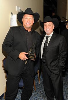 two men standing next to each other wearing black suits and hats, one holding an award