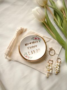 a personalized ring dish and wedding rings on a napkin with flowers in the background