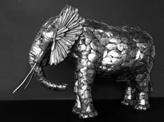 an elephant made out of silver foil on a black surface with its trunk curled up